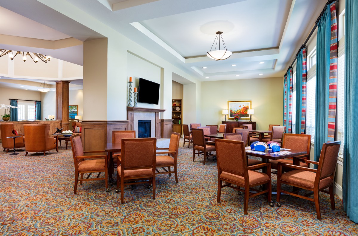 A spacious and well-lit dining room with several tables and chairs, featuring a television and elegant decor.