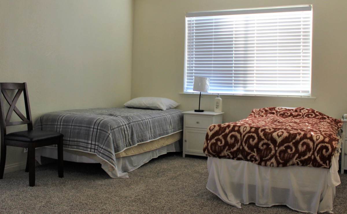 A simple bedroom with two twin beds, a nightstand, and a window.