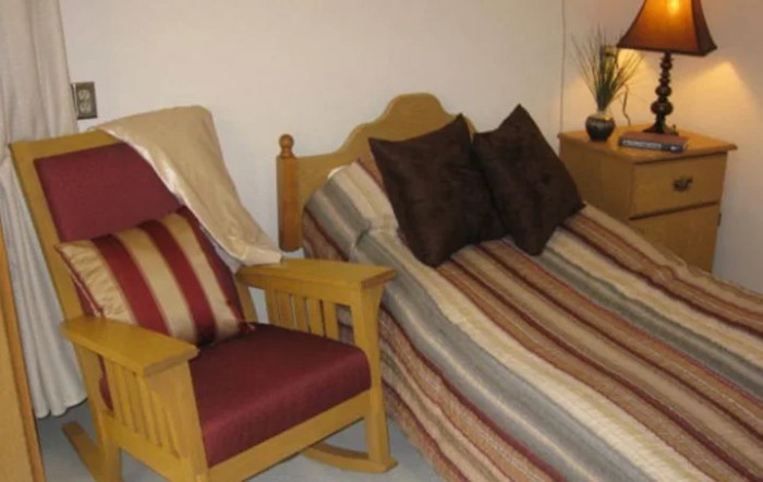 A cozy bedroom featuring a bed with striped bedding and a wooden chair with matching cushions.