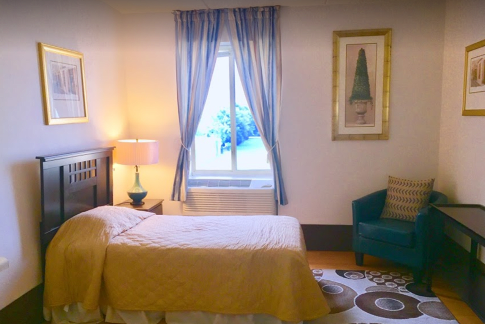 A cozy bedroom with a single bed, a lamp on the nightstand, and a window adorned with curtains.