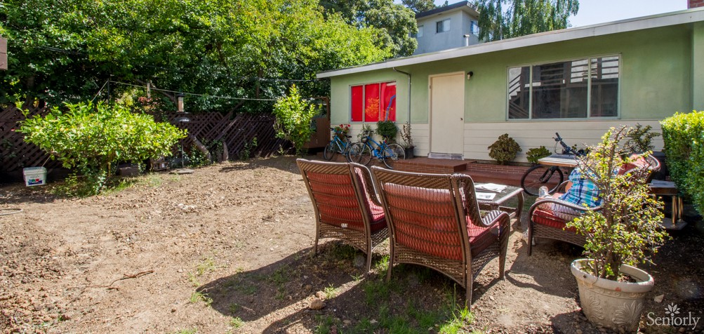 A sunny backyard with wicker chairs facing a small house.