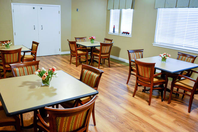 A cozy dining area with neatly arranged tables and chairs, featuring wooden flooring and floral decorations on the tables.