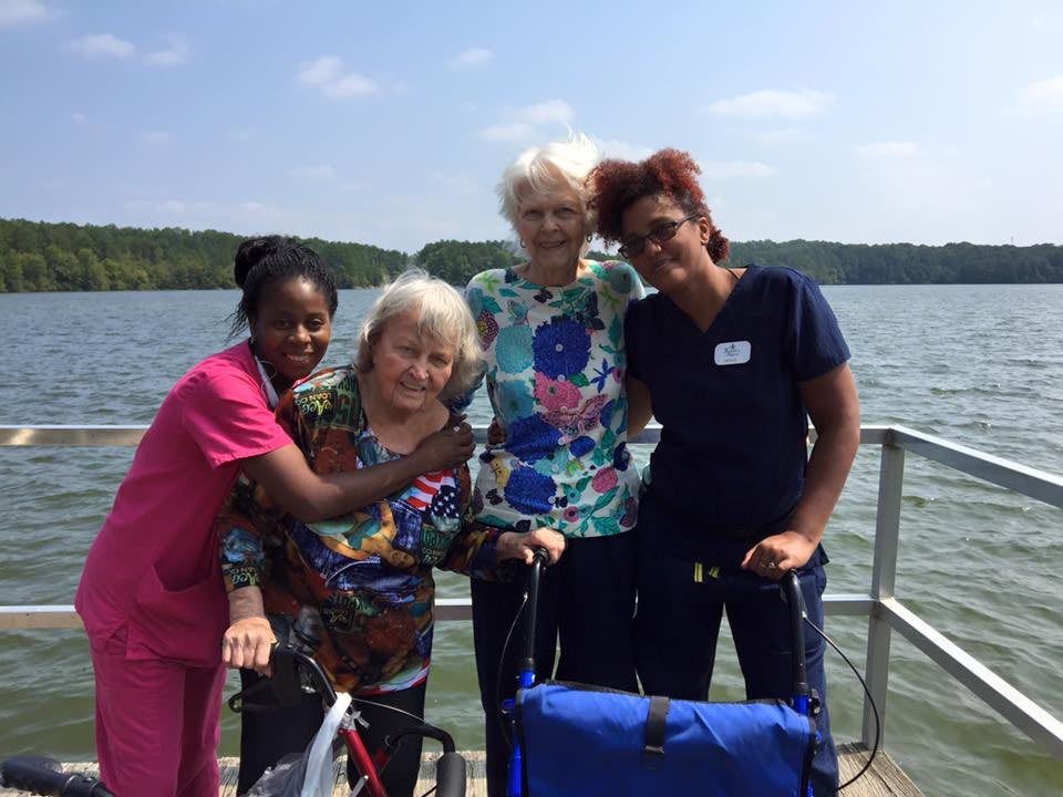 A group of people, including elderly individuals and caregivers, enjoying time by the lake.