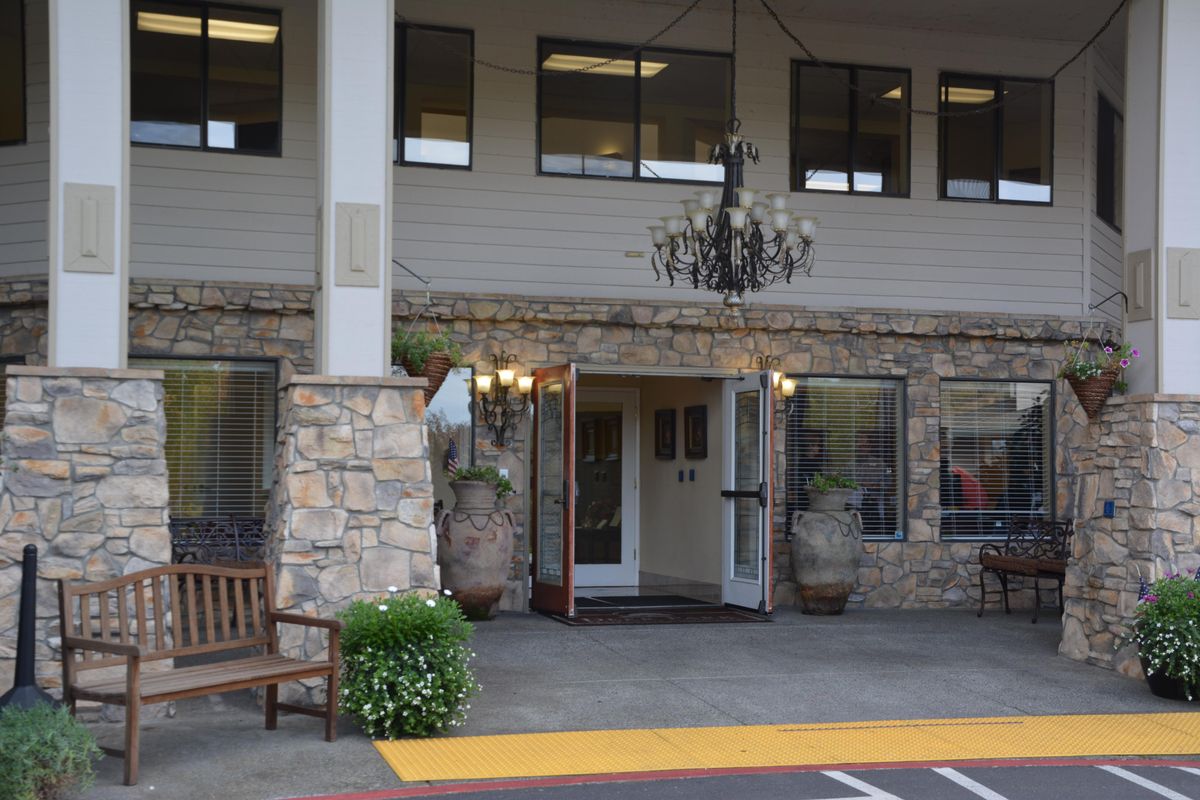 The entrance of a building featuring a stone facade, an outdoor bench, potted plants, and a chandelier.