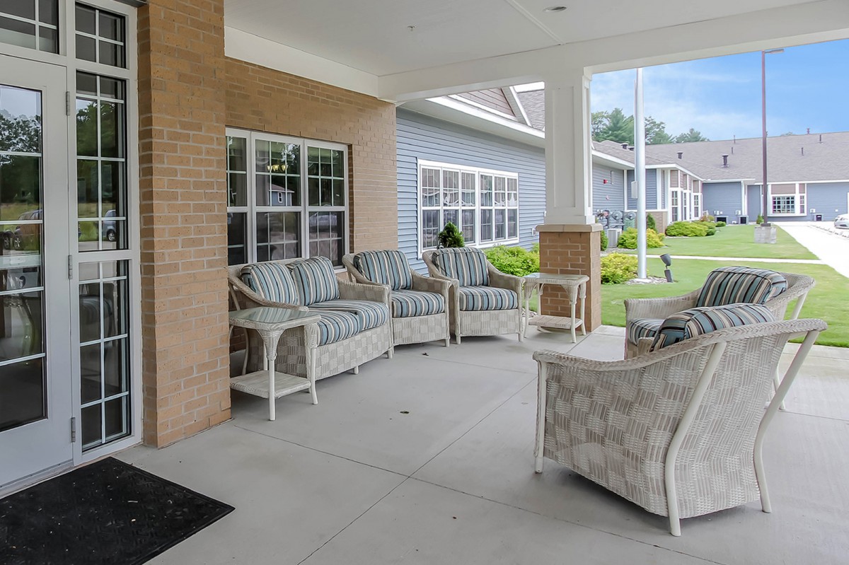 A cozy outdoor porch with cushioned chairs and a table, providing a relaxing seating area outside a building.