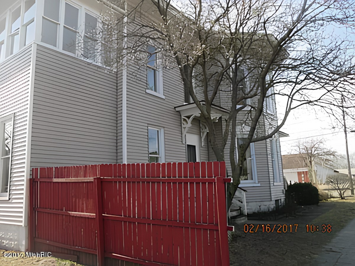 A residential house with a red fence and bare tree in the yard.