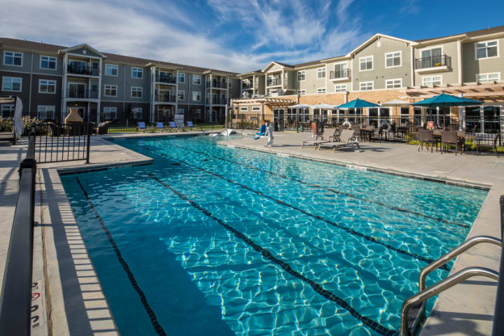 A spacious outdoor swimming pool surrounded by modern apartment buildings on a sunny day.