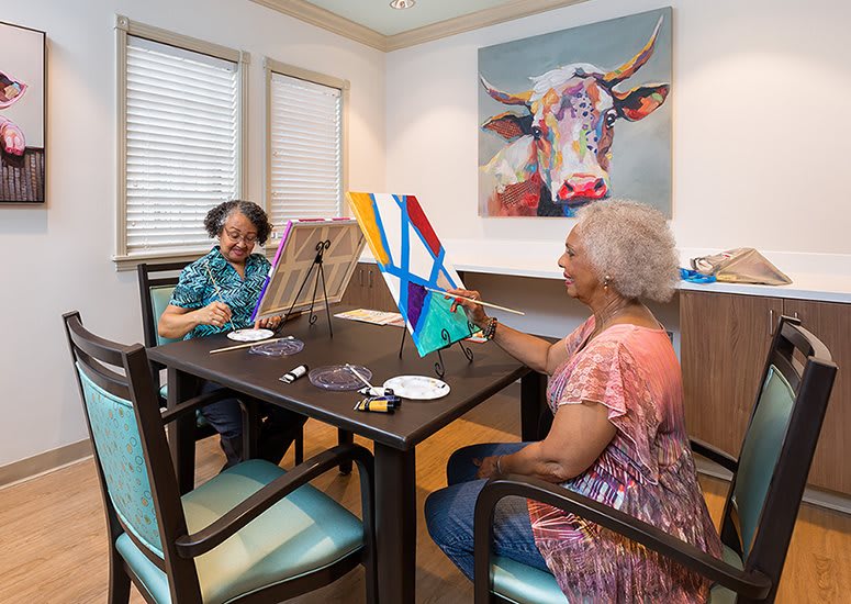 Two senior women enjoying a painting session together indoors.