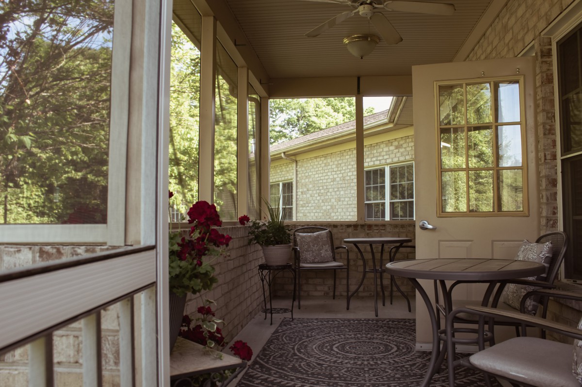 A cozy patio with outdoor seating and plants, illuminated by sunlight.