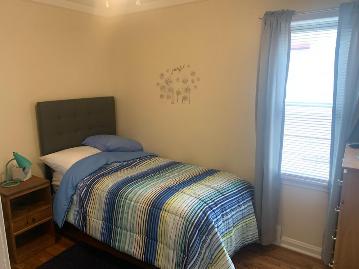 A cozy bedroom with a single bed featuring striped bedding, complemented by a nearby window with curtains.