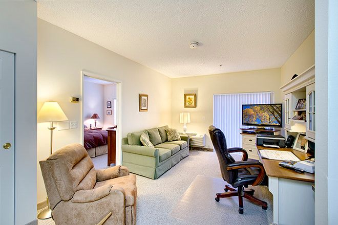 A cozy living room with a sofa, armchair, desk, and television.