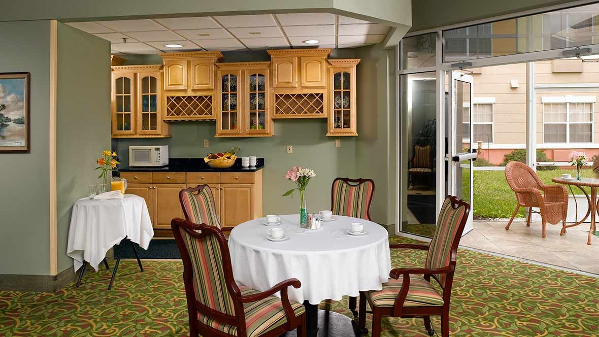 A cozy dining area with a round table set for four, featuring wooden cabinets and a microwave in the background.