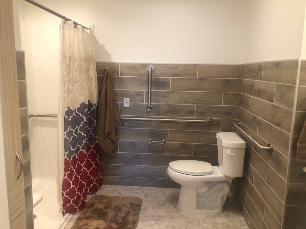 A bathroom with a toilet, shower, and tiled walls, featuring grab bars and a colorful shower curtain.