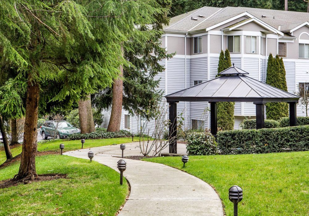 A scenic pathway leading to a gazebo in a residential area, surrounded by lush greenery and trees.