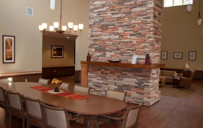 A modern dining room featuring a large stone fireplace, wooden table, and elegant chandelier.