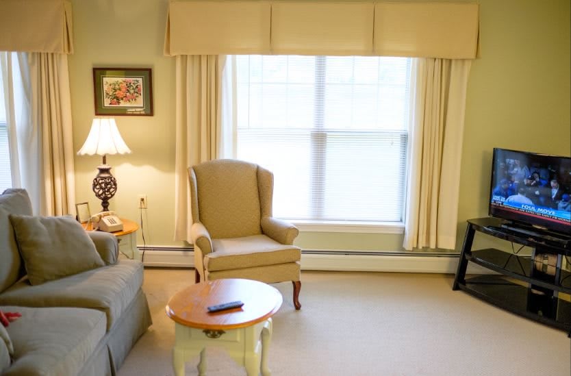 A cozy living room with an armchair, sofa, and a coffee table near a window with curtains.