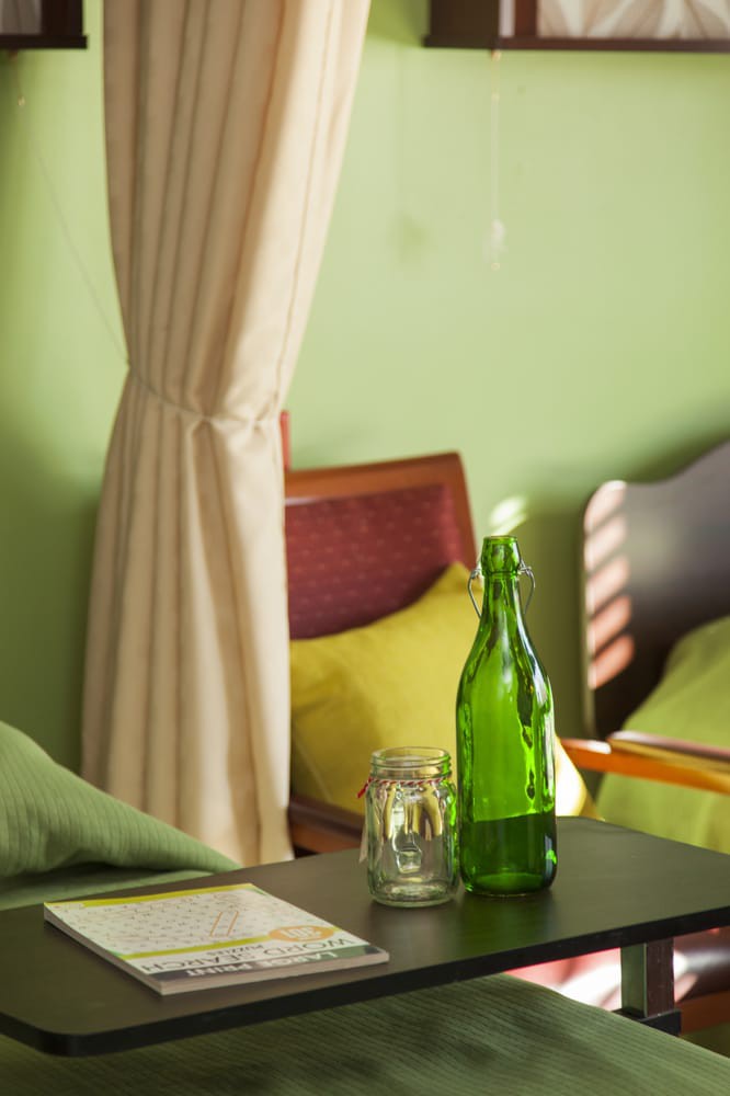 A cozy room with green walls, featuring a green bottle on the table, a chair, and a bed.