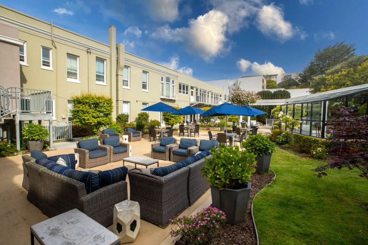 A beautiful outdoor patio area with comfortable seating and blue umbrellas, surrounded by well-maintained gardens.