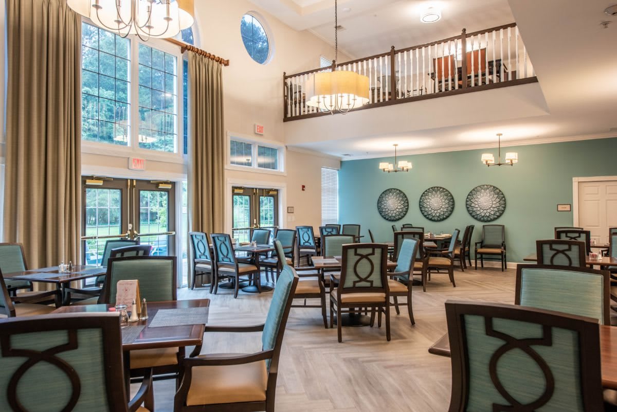 A spacious dining room featuring elegant chandeliers, large windows, and neatly arranged tables and chairs.