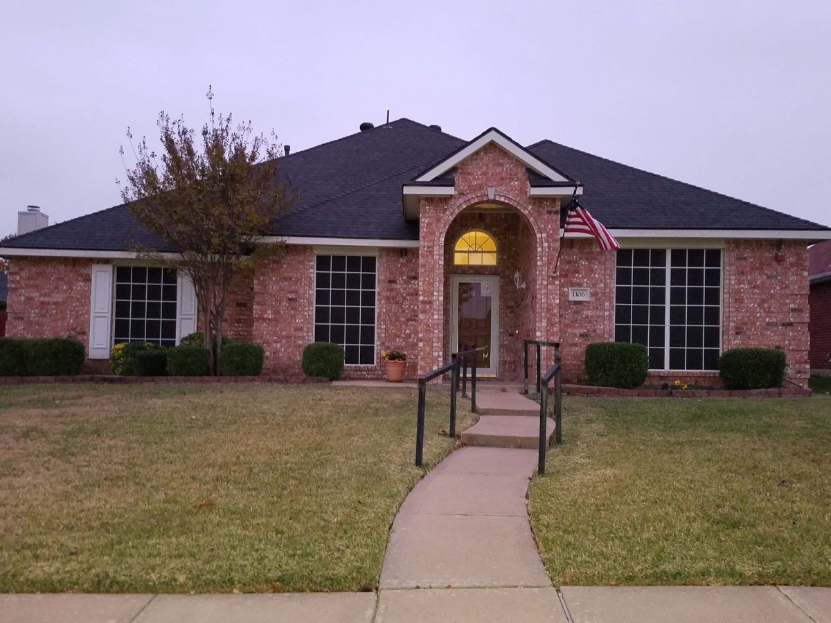 A brick house with a front lawn and an American flag displayed near the entrance.
