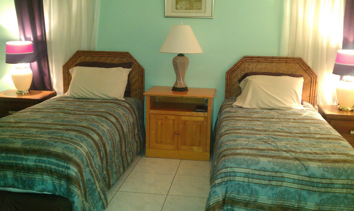 A cozy bedroom with twin beds and a shared nightstand with a lamp.