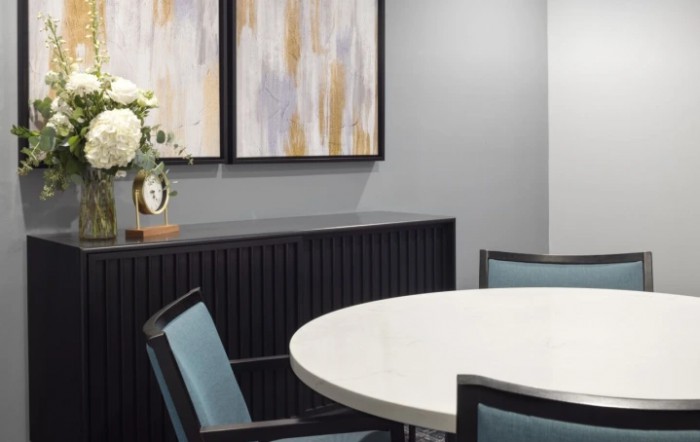 A modern meeting room with a round table, chairs, and abstract artwork on the wall.