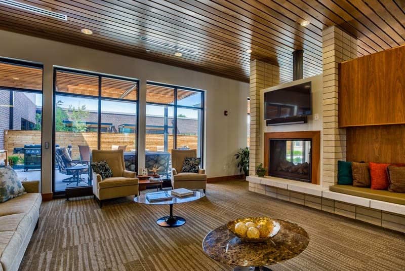 A modern living room with a wooden ceiling, featuring a fireplace and large glass doors leading to the outside.