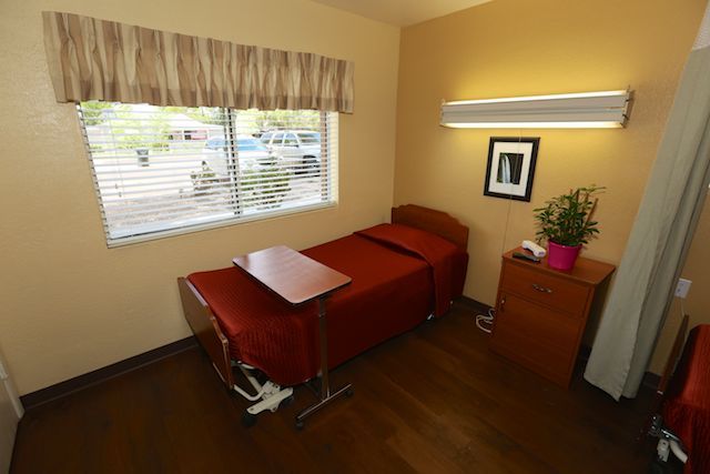 A hospital room with a single bed, side table, and window.