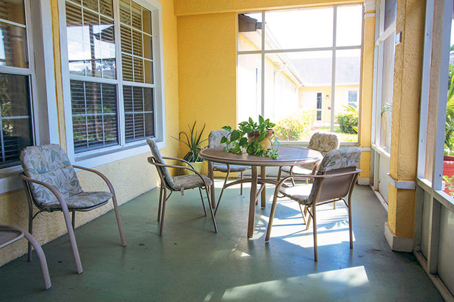 A sunlit patio with a table and chairs, surrounded by yellow walls and plants.