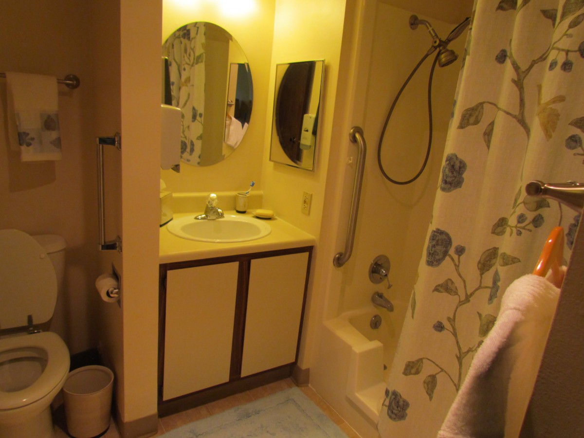 A small bathroom featuring a sink with mirror, shower area with curtain, and storage cabinets.