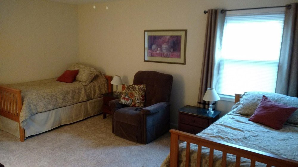 A cozy bedroom featuring two beds, an armchair, nightstands, and a window with curtains.