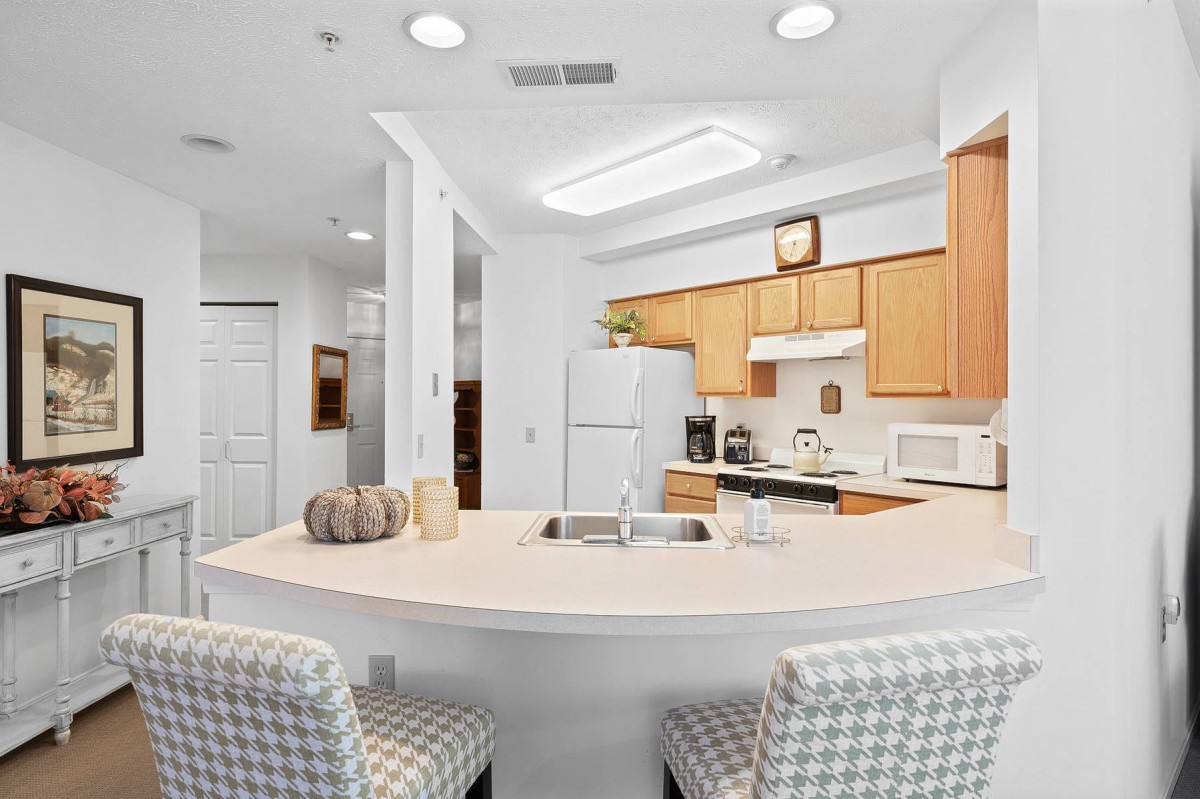 A modern kitchen with wooden cabinets, a white countertop, and seating area.