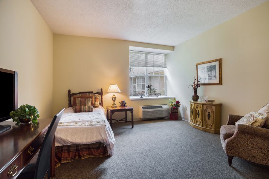 A cozy bedroom with a single bed, a warm lamp on a side table, and a window letting in natural light.