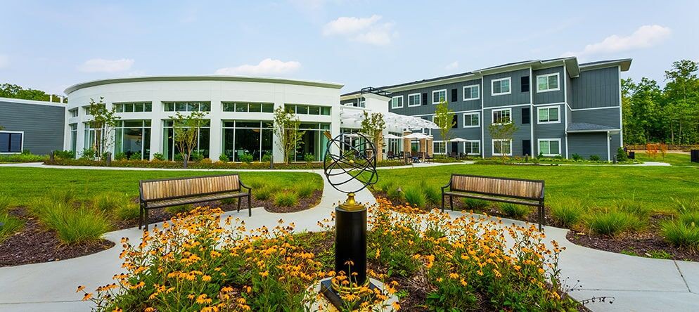 A landscaped garden with benches and a sculpture in front of modern buildings.