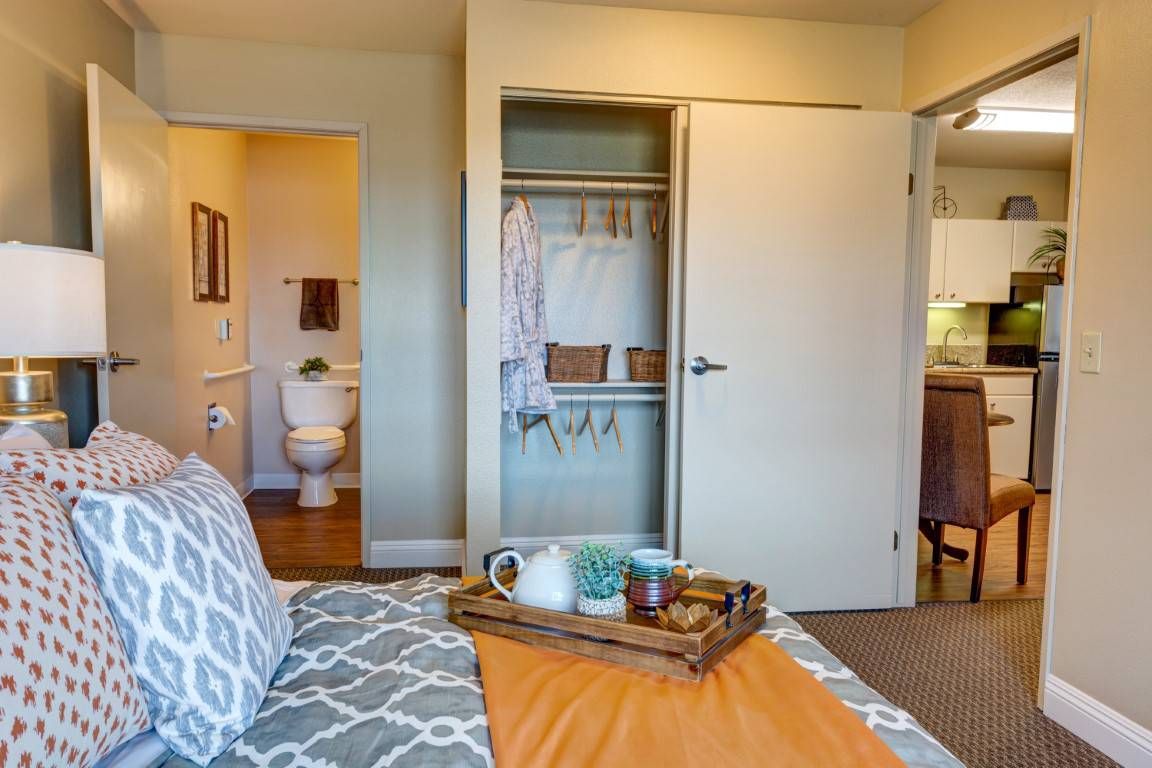A cozy bedroom features a neatly organized closet and an inviting tray on the bed, with a view into the adjoining bathroom.