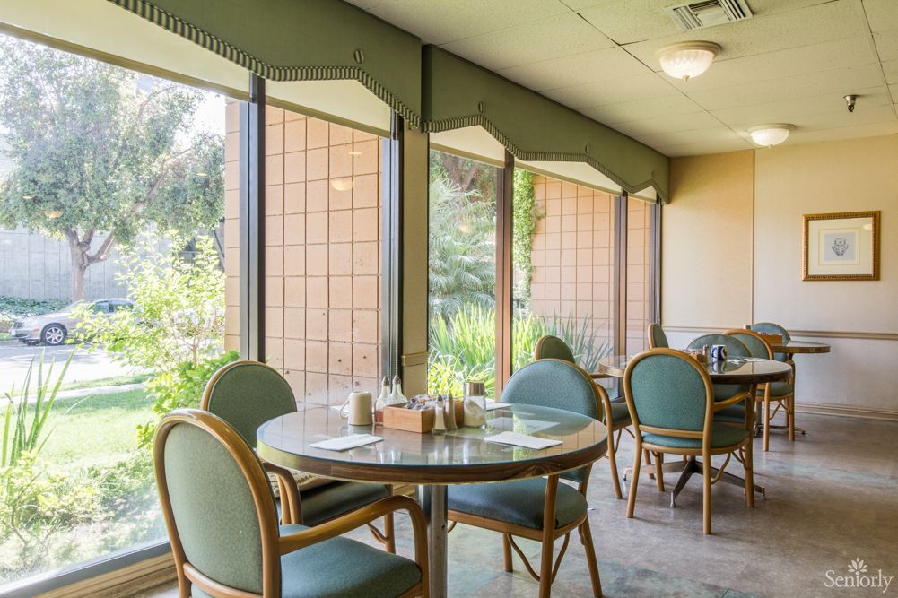 A cozy dining area in a restaurant with tables and chairs by large windows, allowing ample natural light.