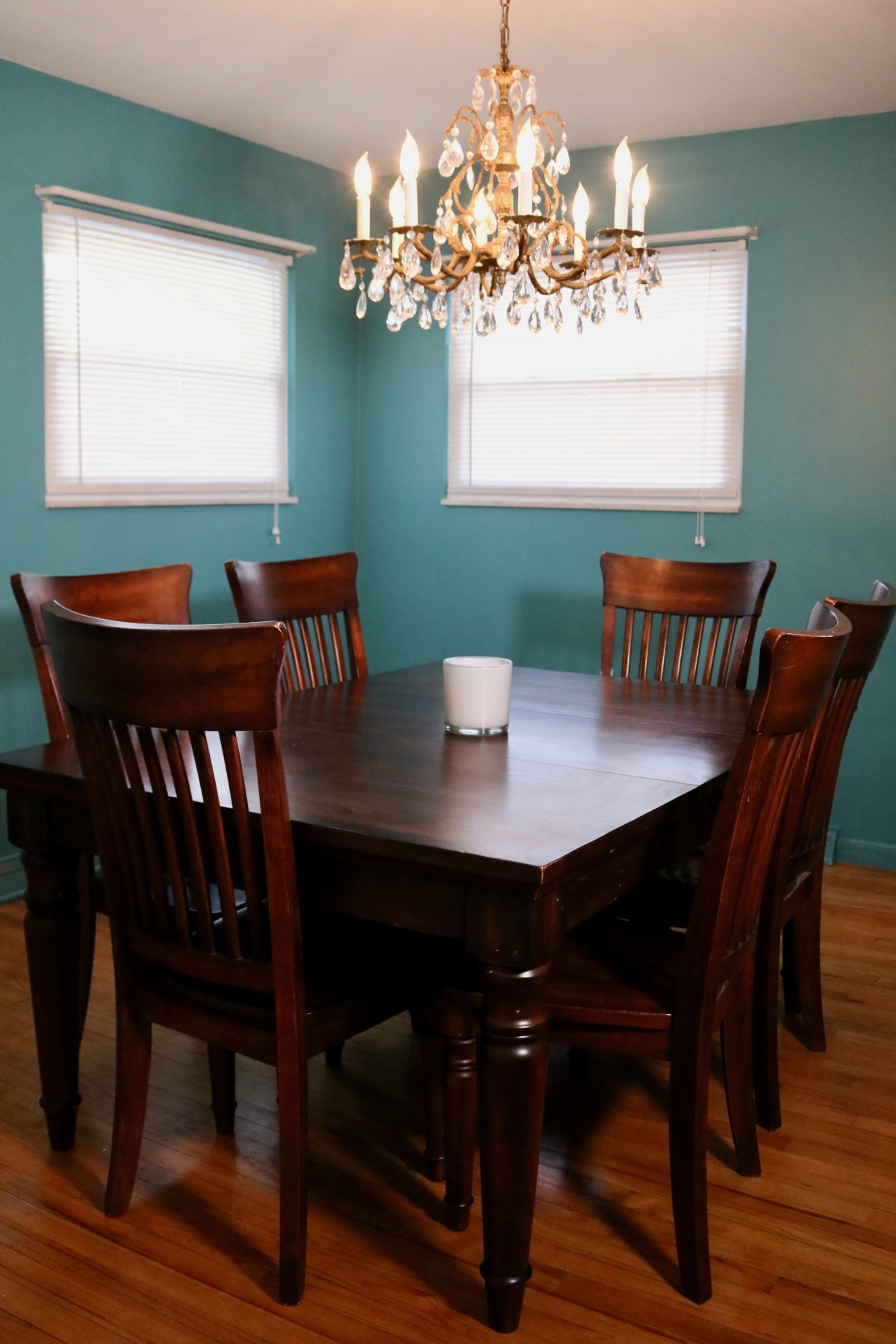 A cozy dining room with a wooden table and chairs, illuminated by a chandelier.