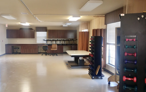 A well-lit modern workspace featuring a large table, ergonomic chair, and organized equipment storage.