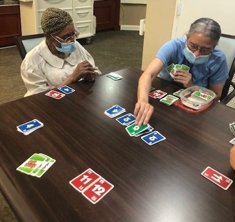 Two people wearing masks play a card game at a table indoors.