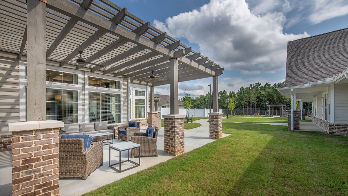 A beautiful outdoor patio with a pergola, furnished with comfortable seating, overlooks a lush lawn on a sunny day.
