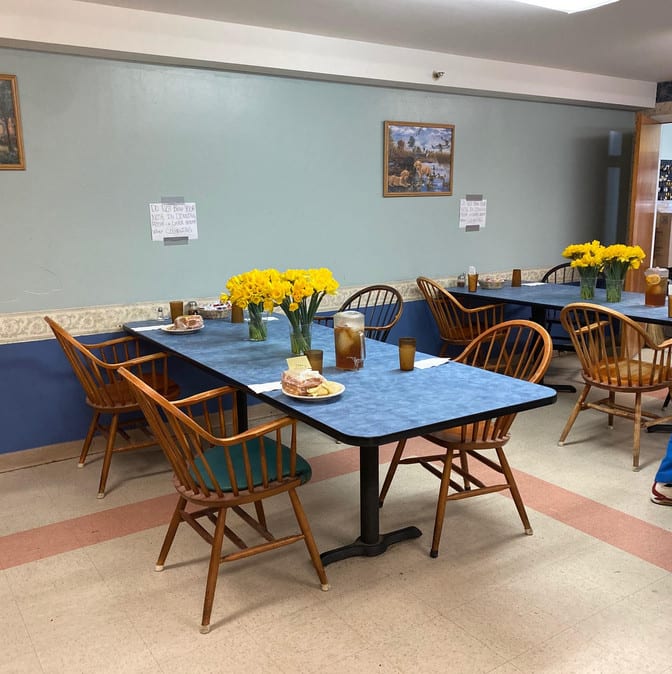 A cozy dining area with arranged tables and chairs, adorned with vases of yellow flowers.