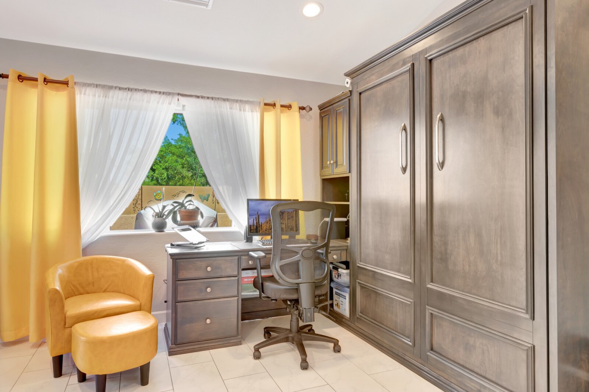 A cozy home office with a desk, chair, and large storage unit, illuminated by natural light from the window.