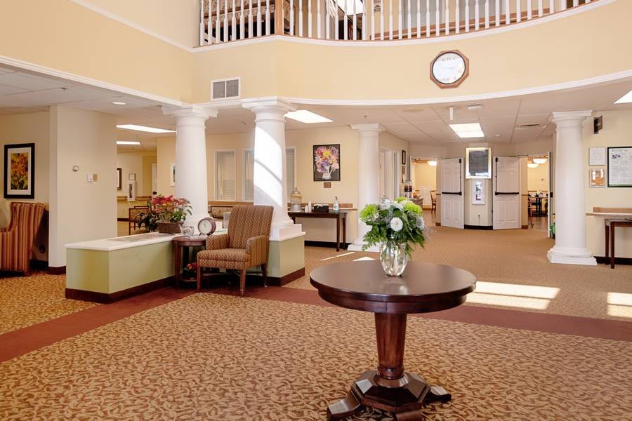 A warm and inviting lobby featuring comfortable seating, a central table with flowers, and carpeted flooring.