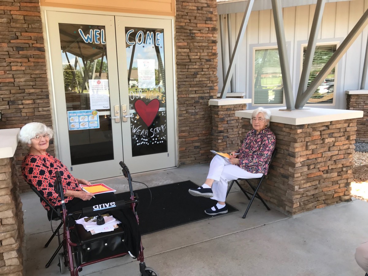 Two seniors seated outside a building entrance enjoying a sunny day.