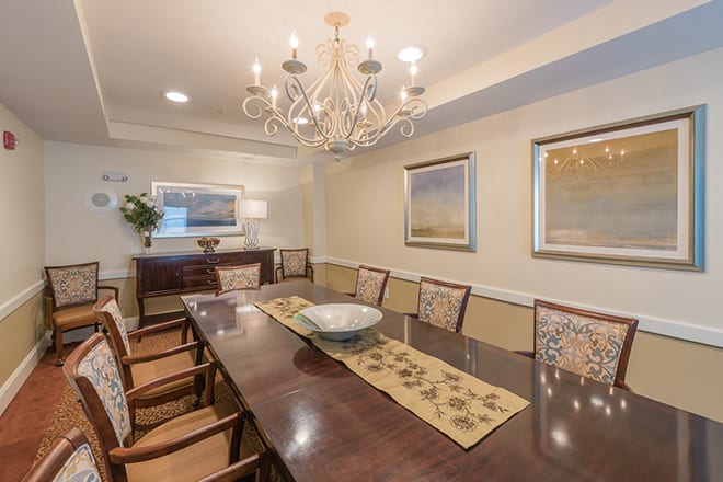 A spacious dining room featuring a large wooden table, elegant chandelier, and framed paintings on the walls.