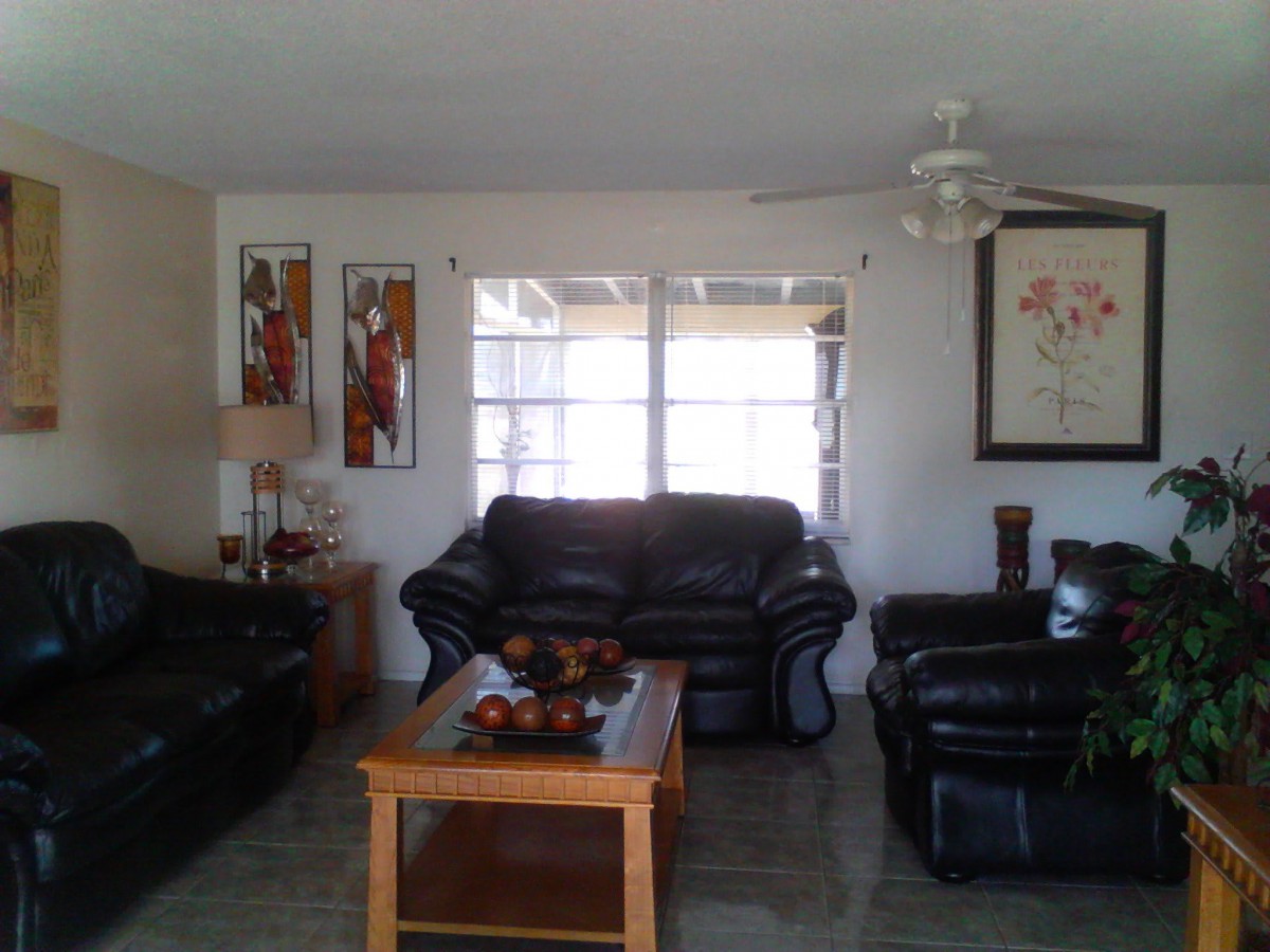 A cozy living room with leather sofas and a wooden coffee table, adorned with artwork and a ceiling fan.