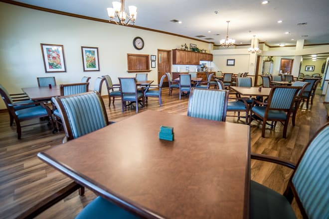 A spacious dining room with multiple tables and chairs, featuring wood flooring and decorative lighting.