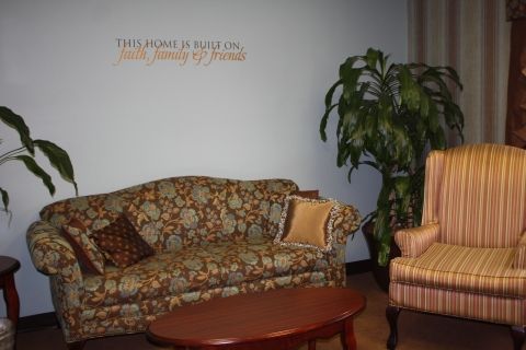 A cozy living room featuring a patterned sofa, an armchair, a potted plant, and a coffee table with wall decor.