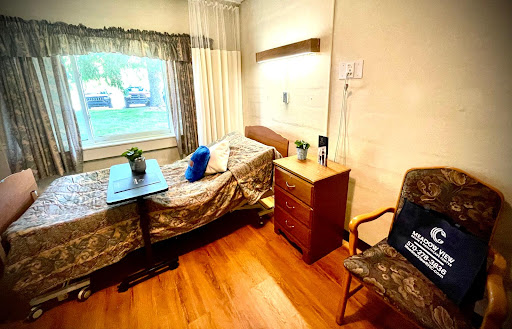 A cozy hospital room featuring a bed, a small table, and a chair by the window.