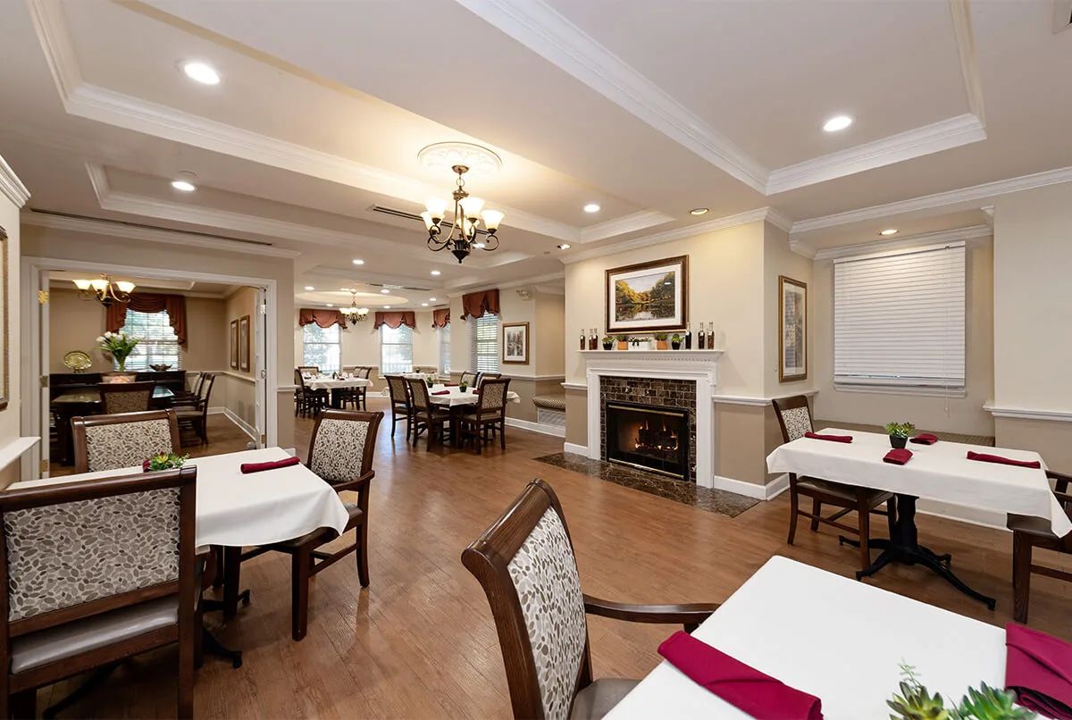 A cozy dining room with neatly arranged tables and chairs, featuring a fireplace and decorated walls.